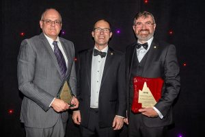 3 men in suits smiling holding awards