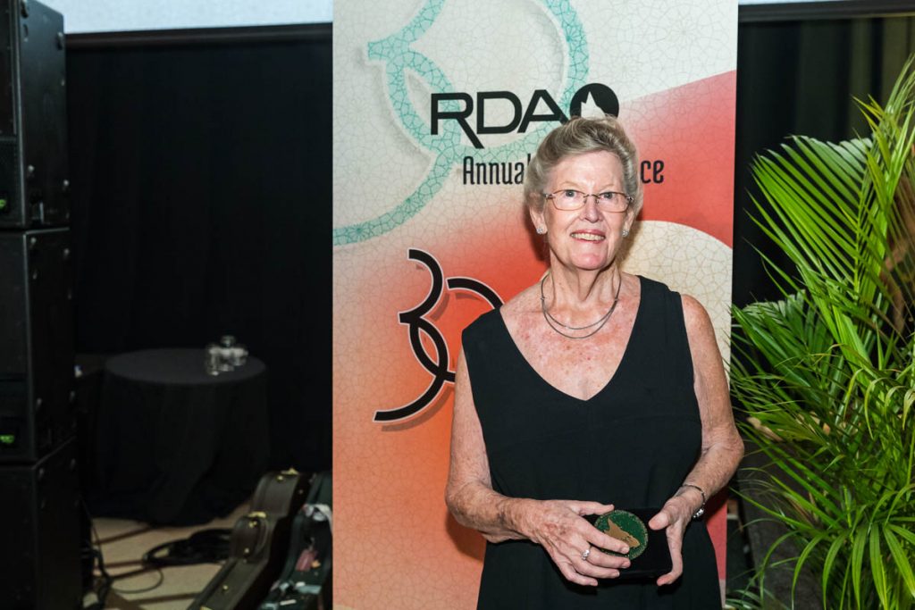 Woman holding an award standing in front of RDAQ Banner